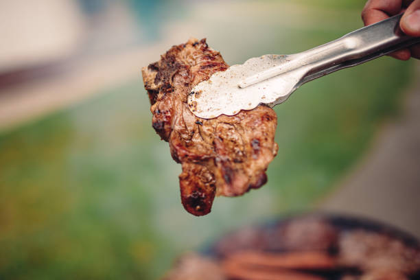 Grilled Pork Chops Close-up photo of men holding grilled pork chops serving tongs stock pictures, royalty-free photos & images