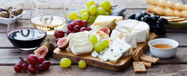 assortimento di formaggi e frutta su tagliere con vino rosso bianco su sfondo legnoso. - cheese antipasto cracker grape foto e immagini stock