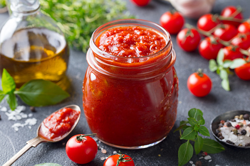 Tomato sauce in a glass jar with fresh herbs, tomatoes and olive oil