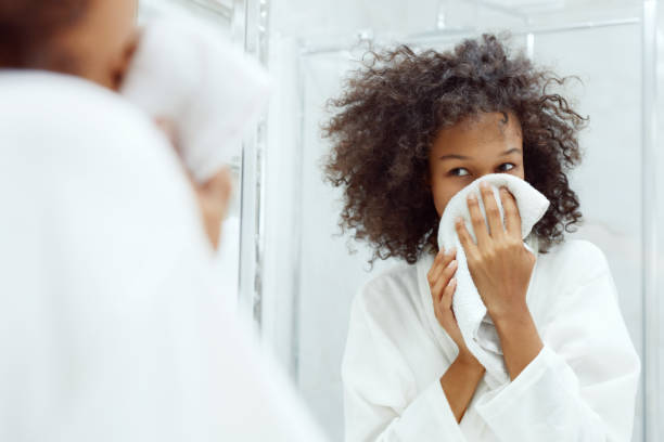 Washing face. Woman drying skin with towel at bathroom Washing face. Closeup of woman drying skin with towel looking in mirror at bathroom. Portrait of beautiful african girl wiping facial skin with soft facial towel woman washing face stock pictures, royalty-free photos & images