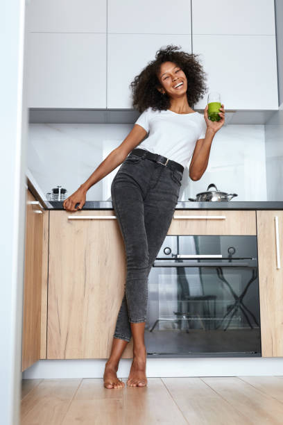 kobieta pije zielony sok detox, napój smoothie w kuchni - vegan food cheerful vertical indoors zdjęcia i obrazy z banku zdjęć