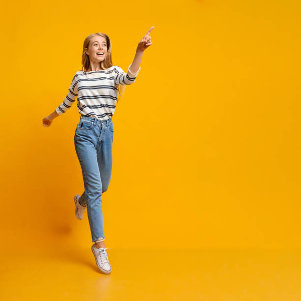 Joyful girl jumping and pointing on copy space on yellow background