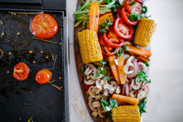 Close up of electrical grill with vegetables on it in the kitchen and big wooden plate with vegan food