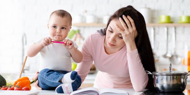 istock Cute baby biting pen, tired mom sitting aside, kitchen interior 1178925529