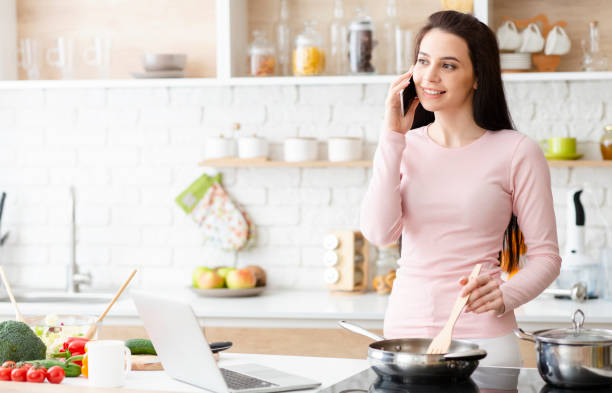 istock Young woman cooking and talking on cellphone at kitchen 1178926759