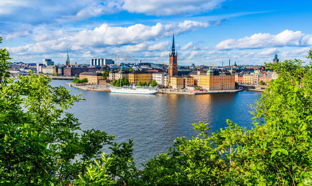Colorful landscape of the old town Gamla Stan island on the waterfront of Lake Malaren as seen from Monteliusvagen hill beyound green trees  with dramatic clouded sky in Stockholm, Sweden Stockholm, Sweden - May 25, 2019: Colorful landscape of the old town Gamla Stan island on the waterfront of Lake Malaren as seen from Monteliusvagen hill beyound green trees  with dramatic clouded sky. lake malaren photos stock pictures, royalty-free photos & images