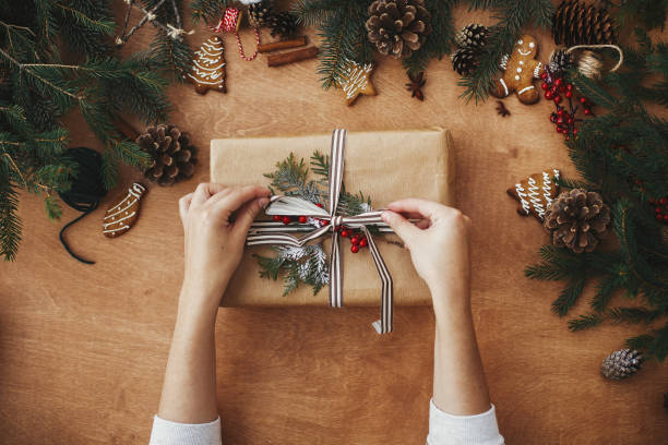 istock Merry Christmas flat lay. Hands holding stylish rustic christmas gift and pine branches, cones, gingerbread cookies,thread, cinnamon, anise on rural wooden table. Seasons greeting 1178928377