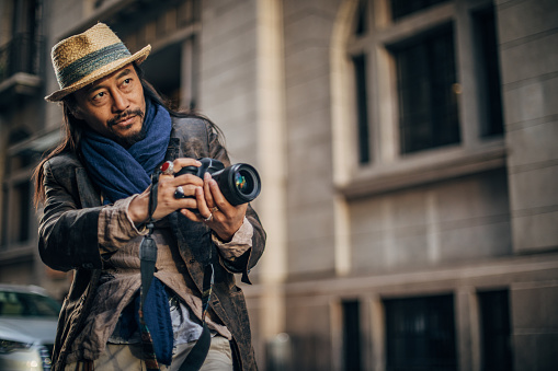 One man, mature Asian guy standing on the city street, photographer taking pictures with camera.