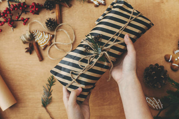 istock Hands holding stylish rustic christmas gift and pine branches, cones, gingerbread cookies,thread, cinnamon, cotton on rural wooden table. Merry Christmas. Season's greeting 1178933604
