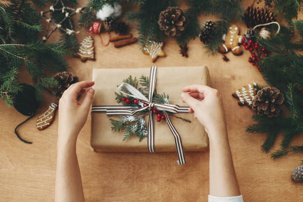 istock Hands holding stylish rustic christmas gift and pine branches, cones, gingerbread cookies,thread, cinnamon, anise on rural wooden table. Seasons greeting. Merry Christmas 1178933736