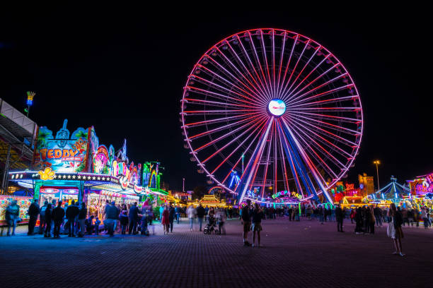 Many people enjoying colorful big wheel and food offers at canstatter wasen oktoberfest folk festival by night stock photo