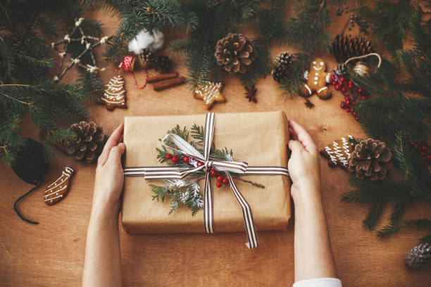 istock Hands holding stylish rustic christmas gift and pine branches, cones, gingerbread cookies,thread, cinnamon, anise on rural wooden table. Seasons greeting. Merry Christmas flat lay 1178934130
