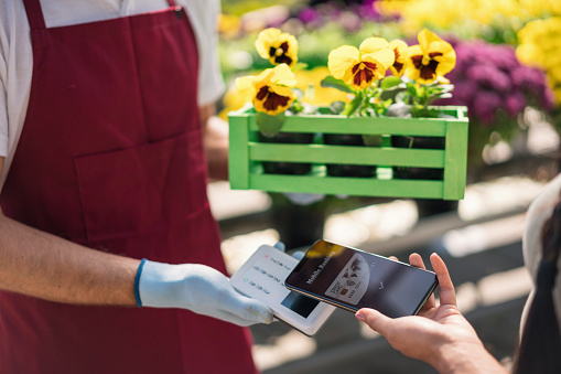 Young woman paying with her mobile phone at the garden center