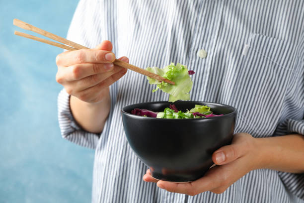 istock Young woman eat salad with chopsticks on blue background, space for text 1178943262