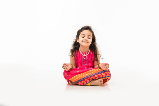 pequeña niña india practicando yoga o meditación con los ojos cerrados, sentado aislado en padmasana sobre fondo blanco - fashion isolated objects beauty and health clothing fotografías e imágenes de stock