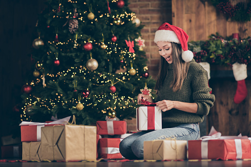 Wow its for me. Full length photo of excited emotional girl sit floor checkered, plaid blanket get gift box for christmas enjoy newyear noel present wear santa claus headwear in house indoors