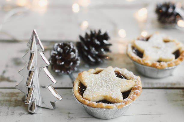 Mince pie on wooden table served with decorative silver christmas tree, pine cones and lights on background. Christmas celebration. New Year and Winter mood