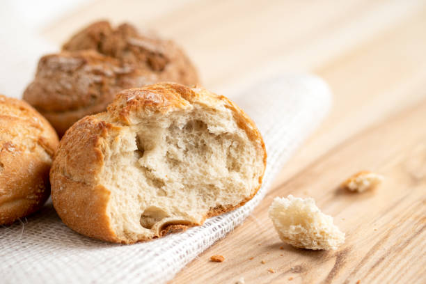 rotolo di pane bianco rustico rotondo rotto accanto a due panini rotondi su tela bianca su legno chiaro. - bread bun broken isolated foto e immagini stock