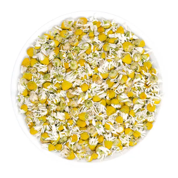 Dried chamomile blossoms in white bowl. Camomile tea, flowers of Matricaria chamomilla, used for herbal infusions and in traditional medicine. Closeup, from above, over white, isolated macro photo.