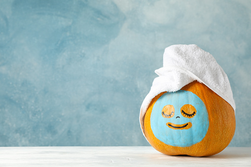 Pumpkin with facial mask and towel on wooden background, copy space