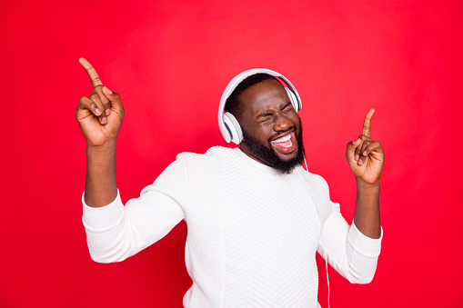 Photo of amazing dark skin man listening favorite playlist in earflaps, enjoy best song moment rhythm wear white knitted sweater isolated red background