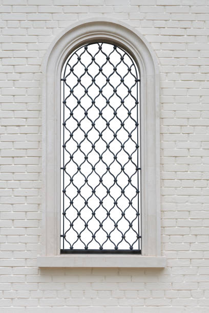 fenêtre arquée avec treillis de fer forgé et figures décoratives dans le mur de briques. fenêtre isolée avec chemin de coupure - cast in stone photos et images de collection