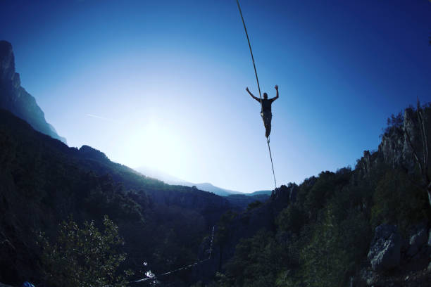 男が伸びたスリングに沿って歩いている。山の中のハイライン。男はバランスをとる自然界の綱渡りのパフォーマンス。山を背景にハイライナー。 - tightrope balance walking rope ストックフォトと画像