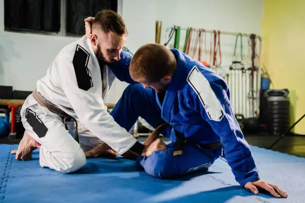 Brazilian Jiu Jitsu BJJ martial arts training sparring at the academy two fighters in butterfly guard position drilling techniques practicing in a gi kimono
