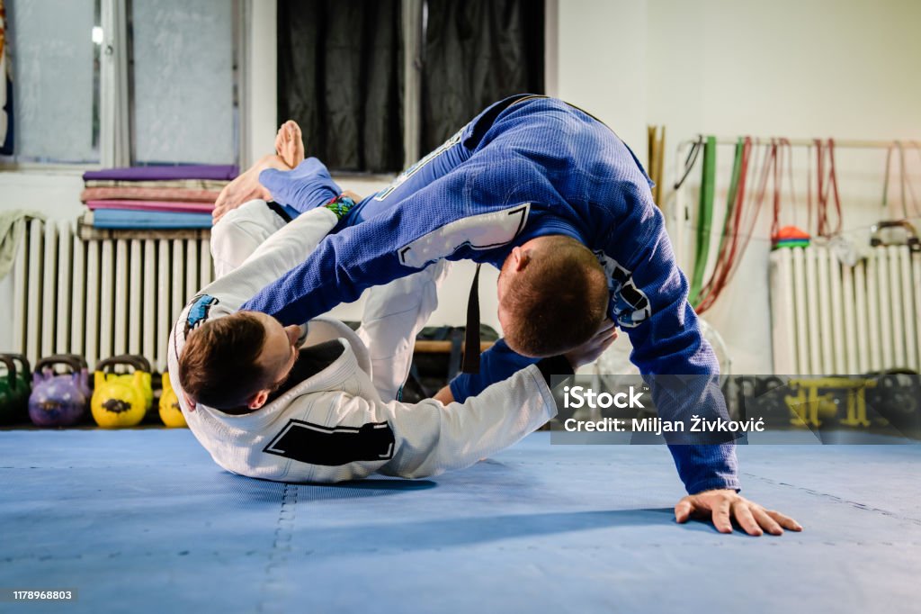 Brazilian Jiu Jitsu BJJ martial arts training sparring at the academy two fighters reverse de la riva guard position drilling techniques practicing in a gi kimono Jujitsu Stock Photo