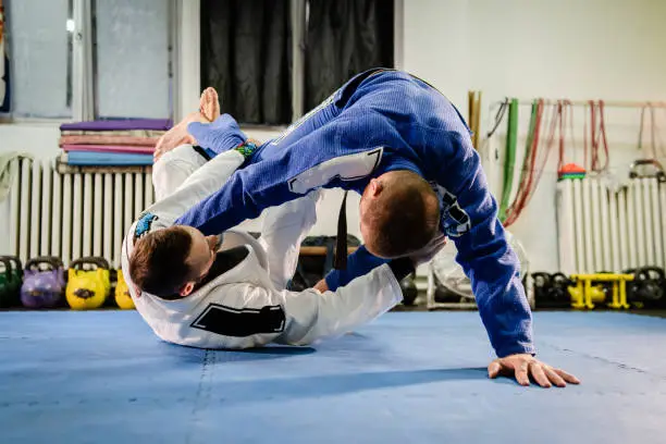 Brazilian Jiu Jitsu BJJ martial arts training sparring at the academy two fighters reverse de la riva guard position drilling techniques practicing in a gi kimono