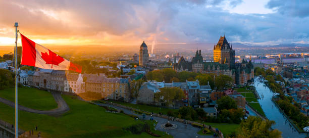 Canadian flag flying over a picturesque Old Quebec City at sunset Aerial panorama view of Old Quebec City. To left side of frame is a Canadian flag in front of a beautiful golden sunset. To the right of the frame is Old Quebec, including the Chateau Frontenac and Defferin Terrace. chateau frontenac hotel stock pictures, royalty-free photos & images