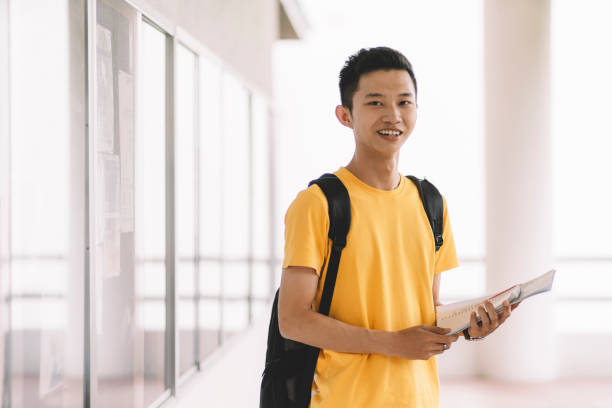 istock an asian chinese male student looking at camera holding text book and carrying a backpack 1178974480
