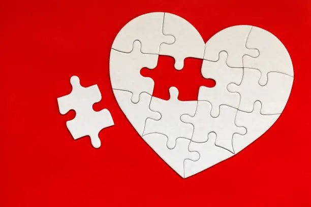 Heart-shaped jigsaw puzzle on color background. Puzzle heart on wooden background. A missing piece of the heart puzzle. Heart shape jigsaw puzzle. Puzzles in the shape of a heart.