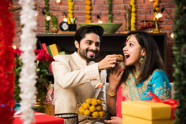 Indian smart couple eating sweet laddu on Diwali or anniversary, selective focus