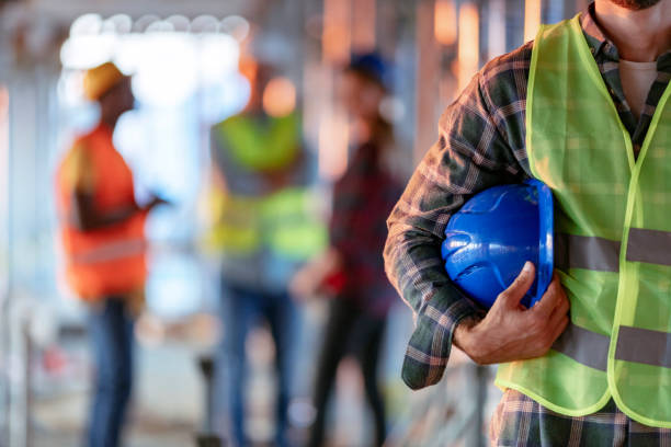 Man holding blue helmet close up Man holding blue helmet close up. Construction man worker with office and people in background. Close up of a construction worker's hand holding working helmet. protective workwear stock pictures, royalty-free photos & images