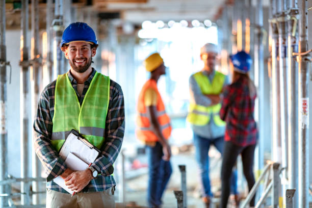 Portrait of a positive Construction Worker Portrait Of young Construction Worker On Building Site looking at the camera with smile. Professional engineer in safety equipment at construction site electrician smiling stock pictures, royalty-free photos & images