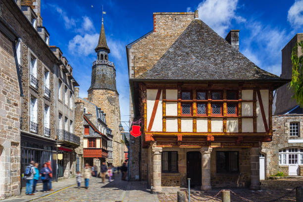 Beautiful view of scenic narrow alley with historic traditional houses and cobbled street in an old town of Dinan with blue sky and clouds. Brittany (Bretagne), France Beautiful view of scenic narrow alley with historic traditional houses and cobbled street in an old town of Dinan with blue sky and clouds. Brittany (Bretagne), France store wall surrounding wall facade stock pictures, royalty-free photos & images