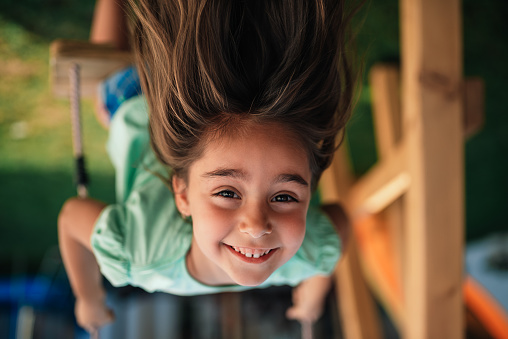 Upside down photo of happy little girl sitting on swing and smiling