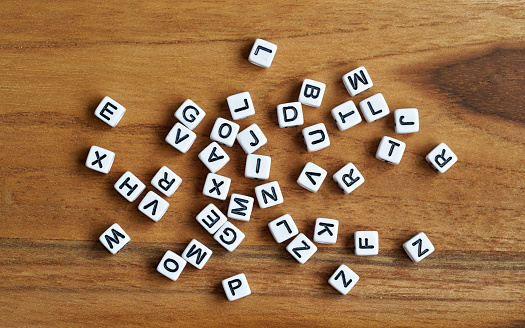 Small white cube beads with various letters scattered on wooden board, view from above.