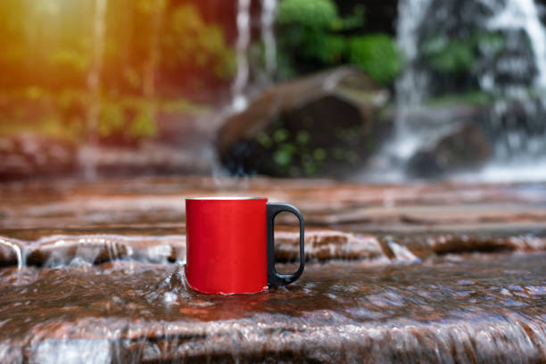 red cup of coffee with waterfall nature background