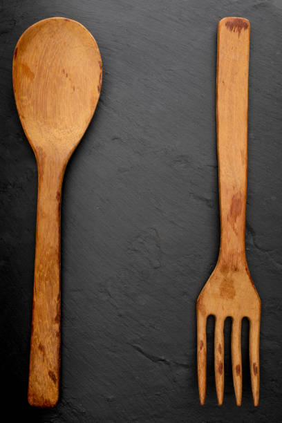 istock Wooden spoon and fork on textured black chalkboard background. Space to insert your text here. Letter for restaurants. (Food concept of spoon, pot). 1178990877