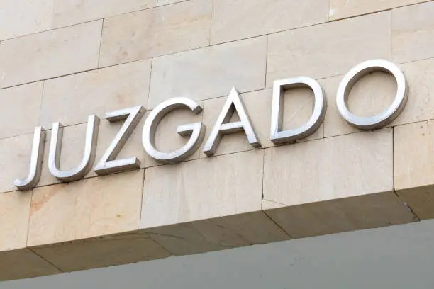 Photo of Word judged in Spanish. Court sign (justice) in metallic letters.