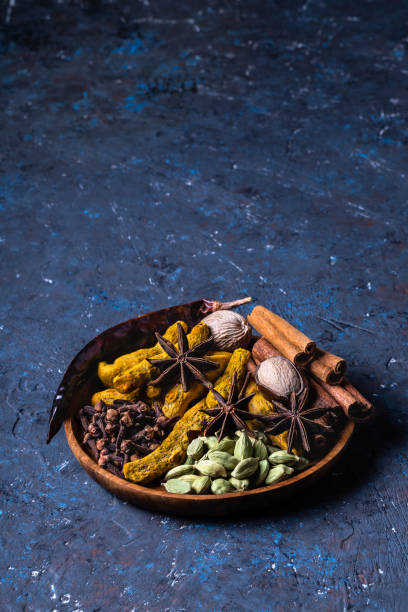 Dry warming Indian spices on plate for autumn winter meal on dark blue concrete background. Dry warming Indian spices for autumn and winter meal on dark blue concrete background. Exotic vitamin, flavor, alternative medicine, Ayurvedic. Turmeric, cinnamon, clove, cardamom, pepper, anise. ayurveda cardamom star anise spice stock pictures, royalty-free photos & images