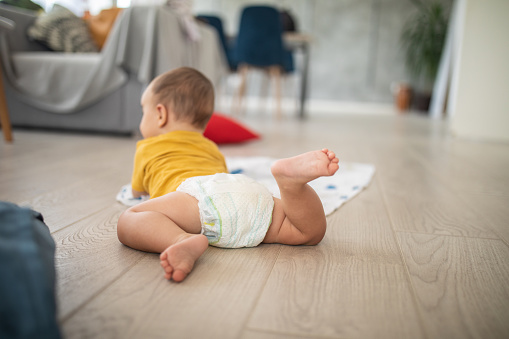 Rear view of baby in diaper crawling on wooden floor at apartment