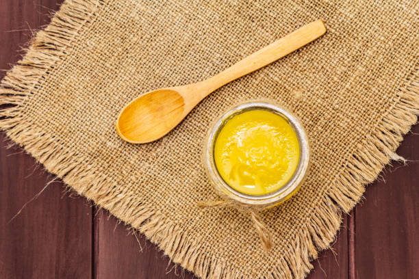 Pure or desi ghee (ghi), clarified melted butter. Healthy fats bulletproof diet concept or paleo style plan Pure or desi ghee (ghi), clarified melted butter. Healthy fats bulletproof diet concept or paleo style plan. Glass jar, wooden spoon on vintage sackcloth. Wooden boards background, copy space top view clarified butter stock pictures, royalty-free photos & images