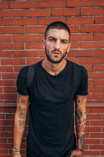 入れ墨を持つ若い男 - tattoo t shirt brick wall portrait ストックフォトと画像