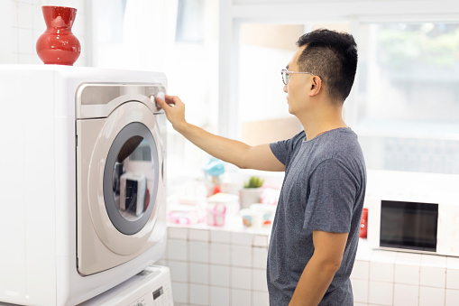 Taiwanese ethnicity man turning on his washing machine and doing some house chores