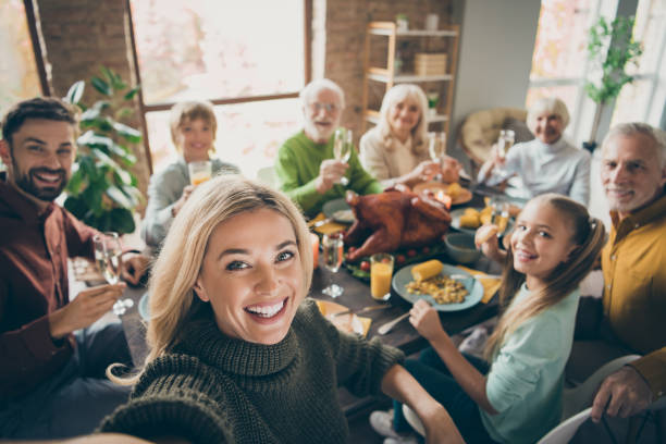 foto van grote familie zitten feest gerechten tabel rond geroosterde kalkoen multi-generatie familieleden maken groeps selfies verhogen wijn glazen sap in woonkamer binnenshuis - avondmaaltijd fotos stockfoto's en -beelden