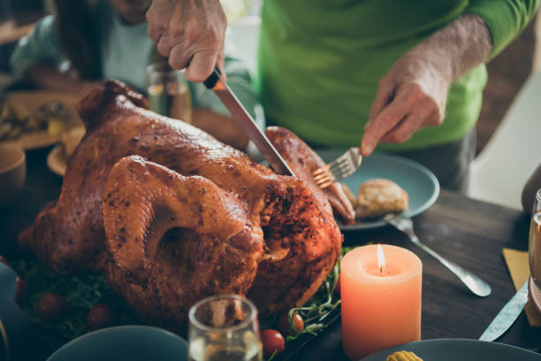 foto ritagliata della festa di famiglia tacchino arrosto sul tavolo nonno mani taglio carne a fette parenti affamati in attesa in soggiorno al chiuso - thanksgiving dinner party feast day turkey foto e immagini stock