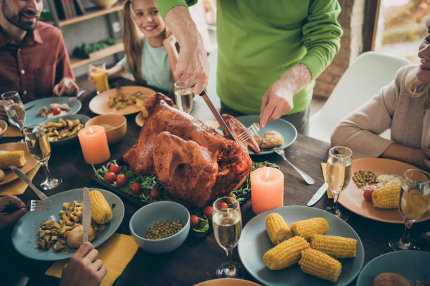 photo cultivée de la table pleine de plats de festin de salle de famille de s'asseoir autour du grand-père rôti de dinde coupant la viande dans des parents affamés de tranches attendant excité dans le salon à l'intérieur - thanksgiving dinner party feast day turkey photos et images de collection